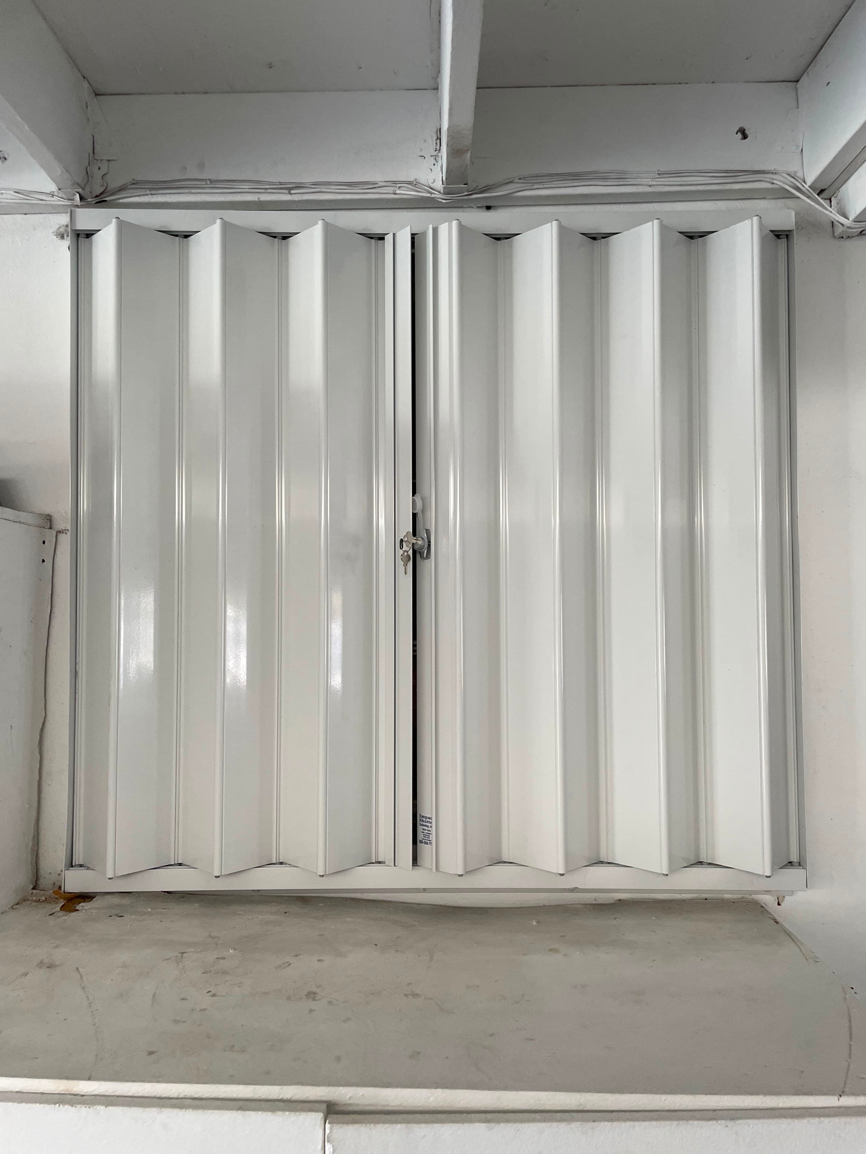 White accordion shutter fully closed and locked at the center posts with upper and lower tracks visible