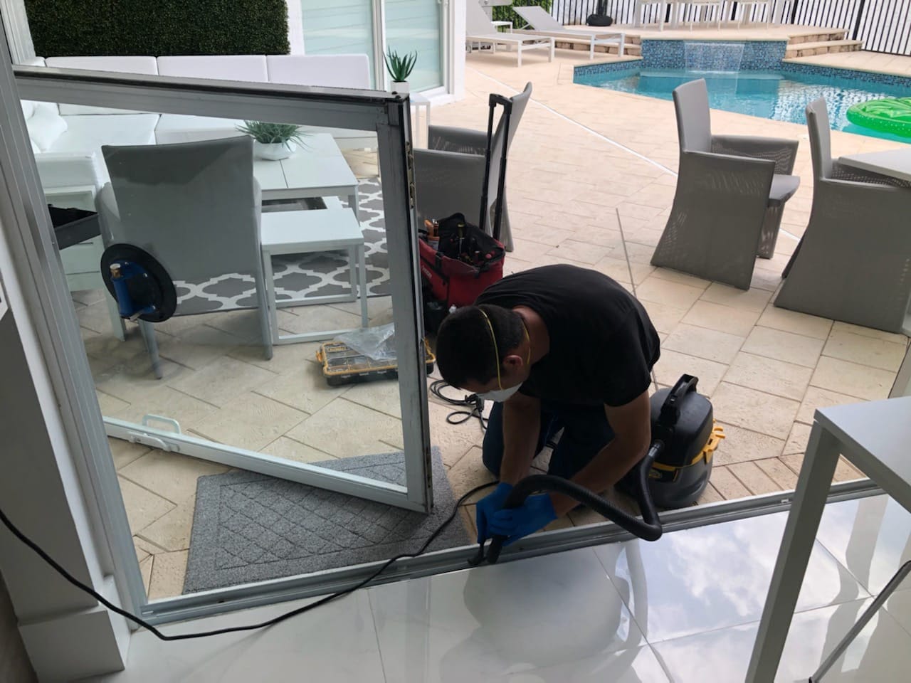 Omega technician cleaning sliding door track with industrial vacuum on poolside patio during track service