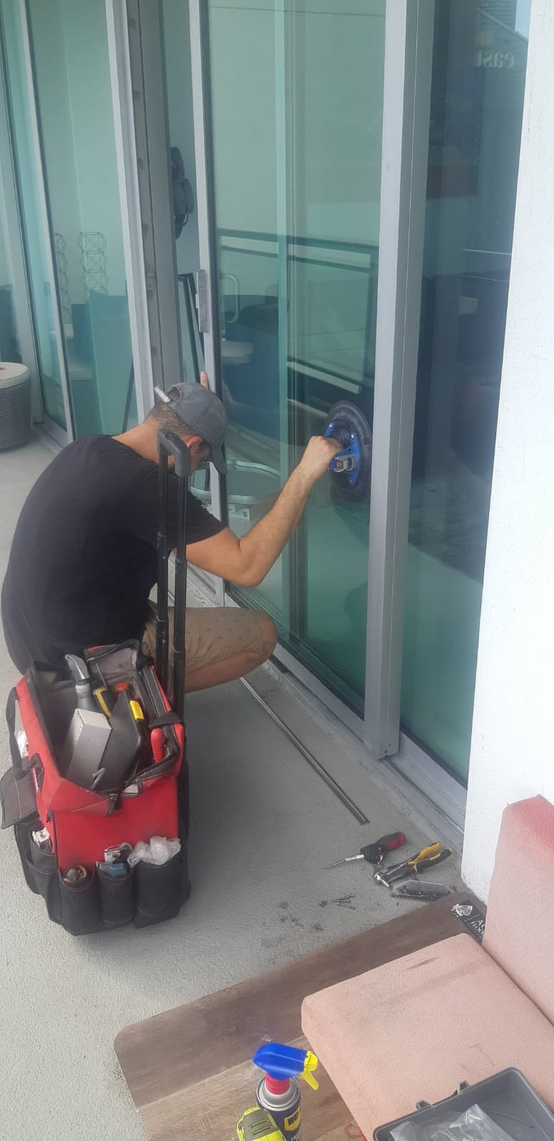 Omega technician using suction cups to seat replacement sliding door glass panel into aluminum frame during poolside install