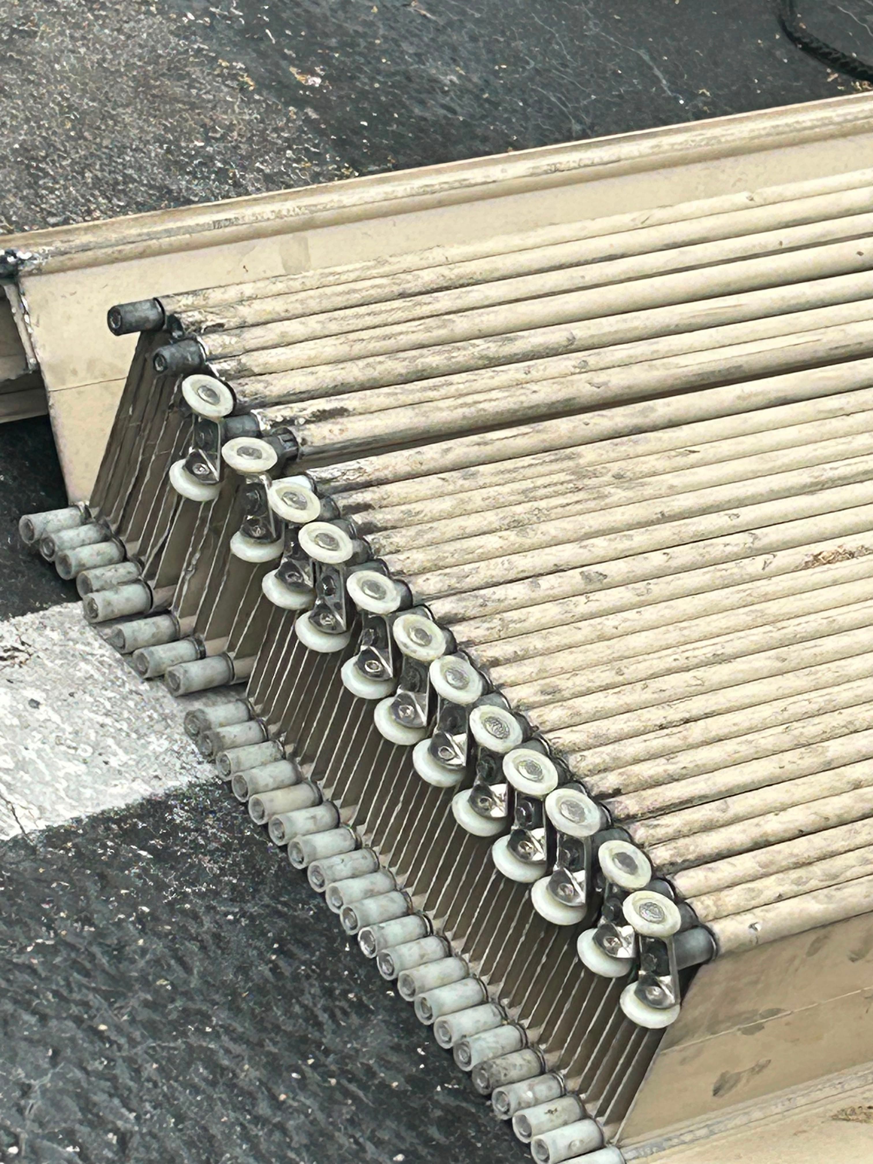 Accordion shutter curtain taken down and laid out on the ground, showing the row of nylon wheel carriers and pivot pins along the blade tops