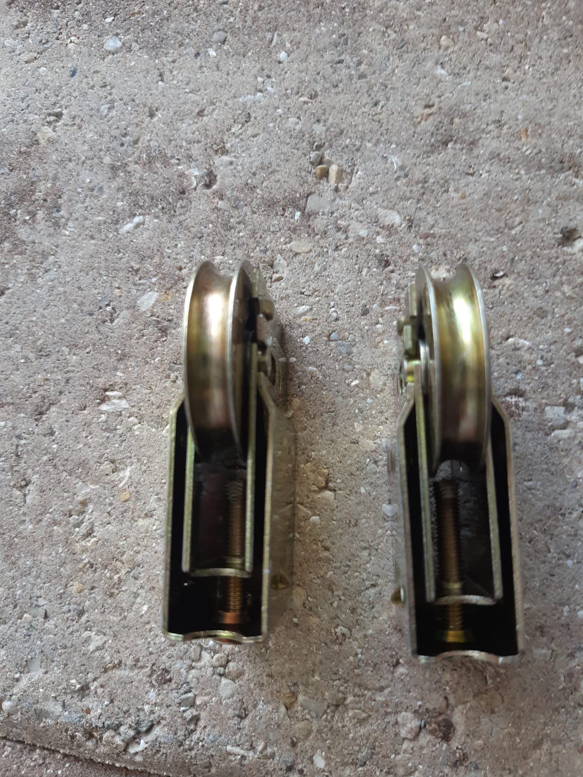 Two brass-coloured sliding door roller assemblies with height-adjustment screws, laid on concrete